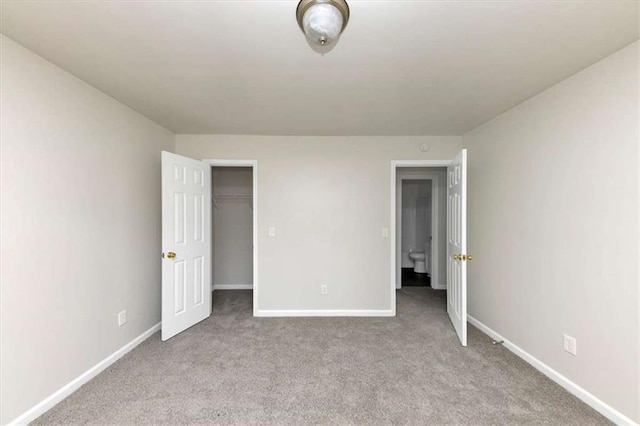 unfurnished bedroom with a walk in closet and light colored carpet