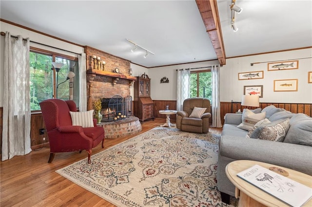 living room with crown molding, hardwood / wood-style floors, wooden walls, track lighting, and a brick fireplace