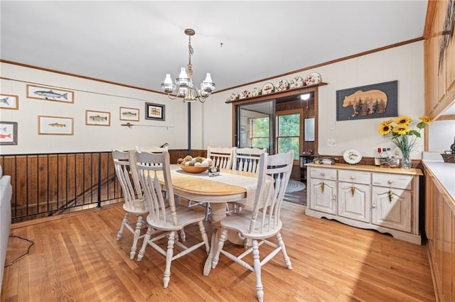 dining area with crown molding, wooden walls, an inviting chandelier, and light wood-type flooring