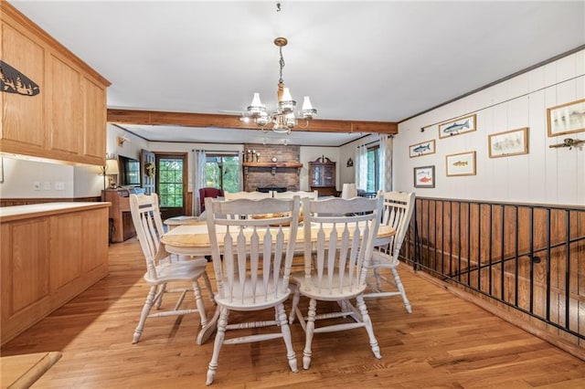 dining space featuring beamed ceiling, a brick fireplace, a chandelier, and light hardwood / wood-style floors