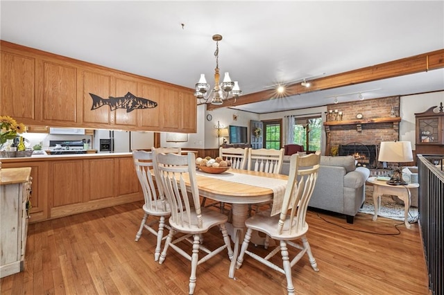 dining area featuring beamed ceiling, a brick fireplace, a notable chandelier, and light wood-type flooring