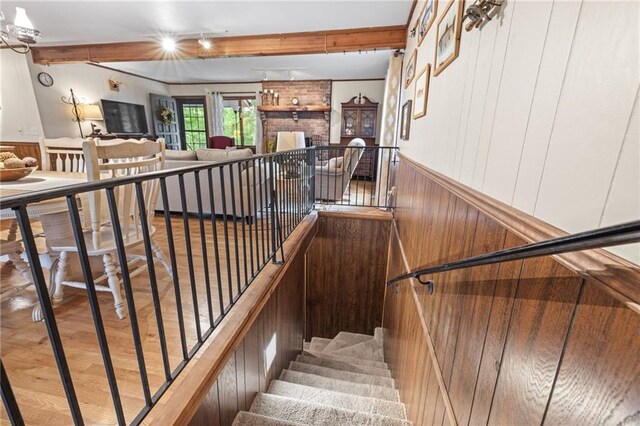 stairway featuring beamed ceiling, hardwood / wood-style flooring, a fireplace, and wood walls