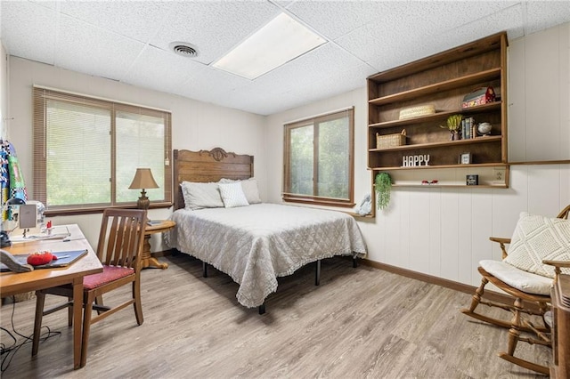 bedroom featuring multiple windows, a paneled ceiling, and light wood-type flooring