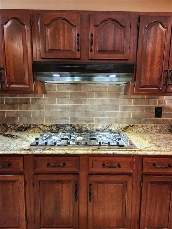 6210 Douglas Manor Ct, Douglasville, GA 30134 - kitchen with under cabinet range hood, stainless steel gas cooktop, tasteful backsplash, and light stone counters
