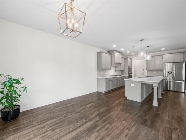 kitchen with stainless steel appliances, decorative backsplash, hanging light fixtures, gray cabinets, and a kitchen island with sink