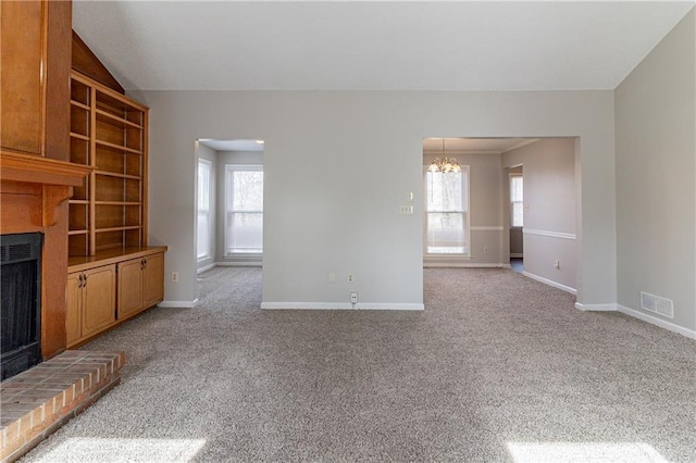 unfurnished living room featuring a brick fireplace, light colored carpet, a chandelier, and a healthy amount of sunlight