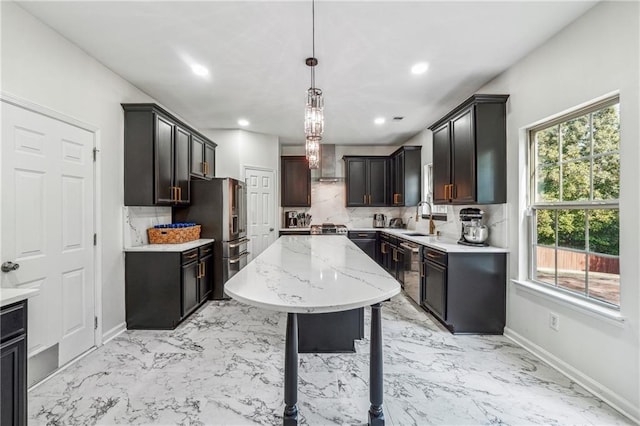 kitchen featuring marble finish floor, stainless steel appliances, backsplash, a sink, and wall chimney exhaust hood