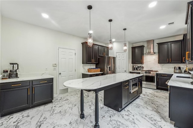 kitchen with marble finish floor, appliances with stainless steel finishes, a kitchen island, and wall chimney range hood