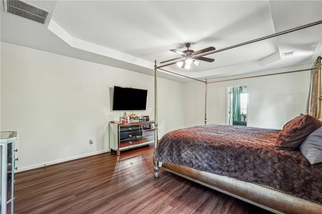 bedroom with a tray ceiling, wood finished floors, visible vents, and baseboards