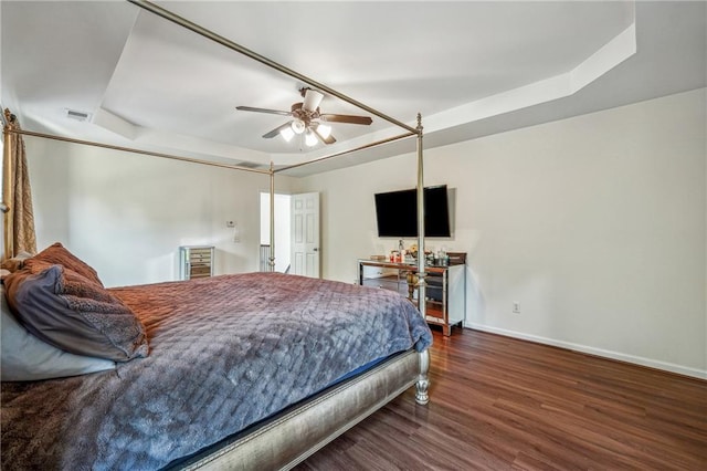 bedroom with a raised ceiling, visible vents, ceiling fan, wood finished floors, and baseboards