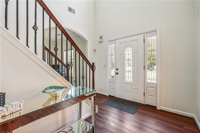 entrance foyer with a towering ceiling, wood finished floors, visible vents, and baseboards