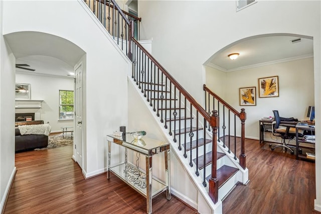 staircase featuring arched walkways, wood finished floors, visible vents, ornamental molding, and a glass covered fireplace