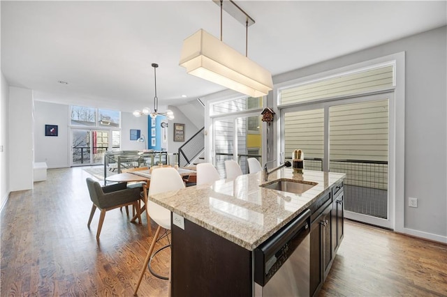 kitchen with wood finished floors, a sink, a notable chandelier, pendant lighting, and stainless steel dishwasher