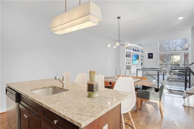 kitchen with a breakfast bar area, light wood finished floors, stainless steel dishwasher, a sink, and light stone countertops