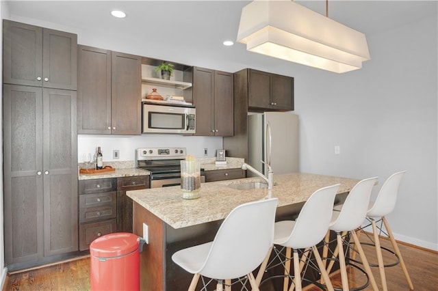 kitchen with a kitchen island with sink, recessed lighting, stainless steel appliances, wood finished floors, and a sink