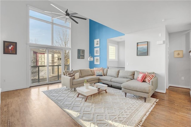 living area featuring a ceiling fan, wood finished floors, a towering ceiling, and baseboards