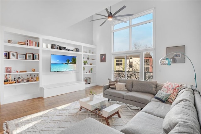 living room featuring a high ceiling, wood finished floors, a ceiling fan, and built in features