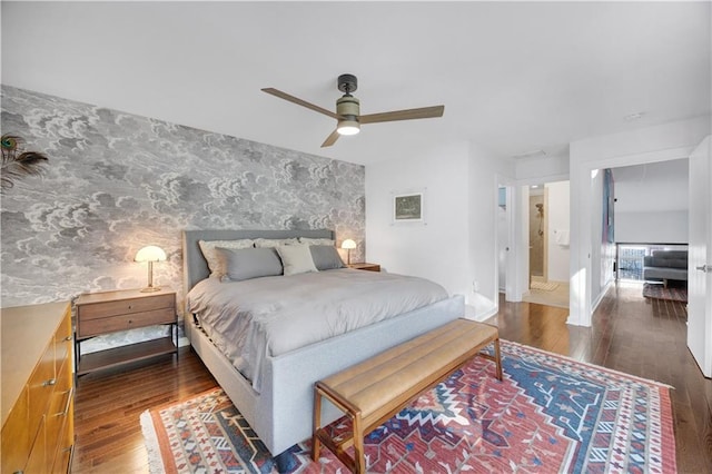 bedroom featuring wallpapered walls, an accent wall, baseboards, and wood finished floors