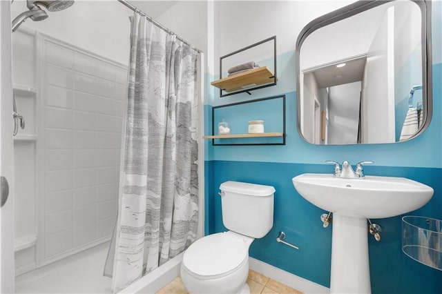 bathroom featuring curtained shower, toilet, a sink, baseboards, and tile patterned floors