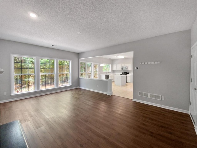 unfurnished living room with hardwood / wood-style floors, a healthy amount of sunlight, and a textured ceiling