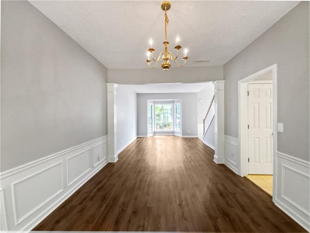 unfurnished dining area with dark hardwood / wood-style flooring, a textured ceiling, decorative columns, and a notable chandelier