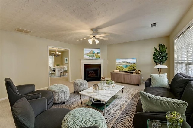 living room featuring ceiling fan with notable chandelier, a textured ceiling, and light carpet