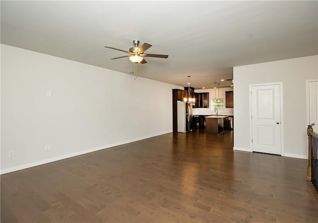 unfurnished living room featuring ceiling fan with notable chandelier and dark hardwood / wood-style flooring