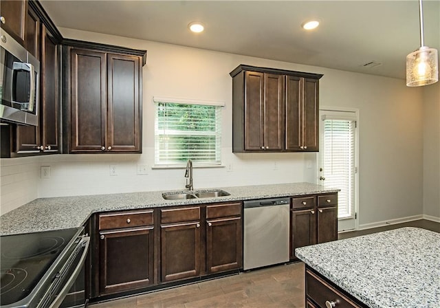 kitchen with sink, dark brown cabinets, light stone countertops, stainless steel appliances, and pendant lighting