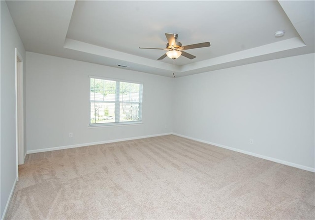 carpeted spare room with a tray ceiling and ceiling fan