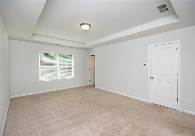 empty room featuring a tray ceiling and light carpet