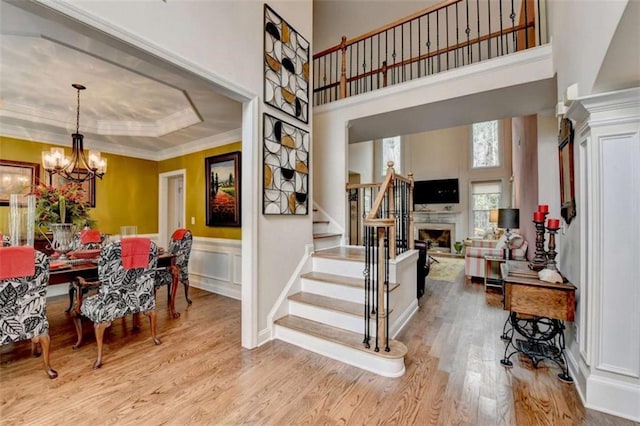 interior space with a fireplace, wood finished floors, stairs, ornamental molding, and an inviting chandelier