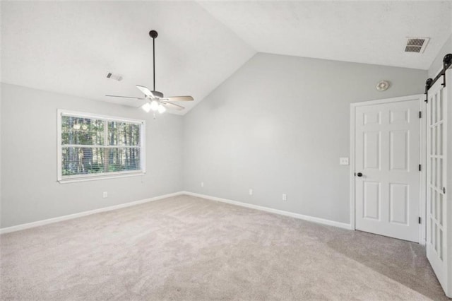 carpeted spare room with ceiling fan, a barn door, and lofted ceiling