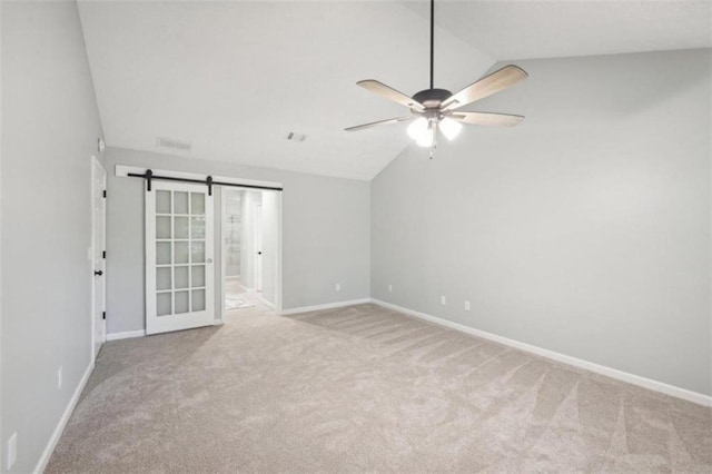 spare room featuring ceiling fan, a barn door, light carpet, and lofted ceiling