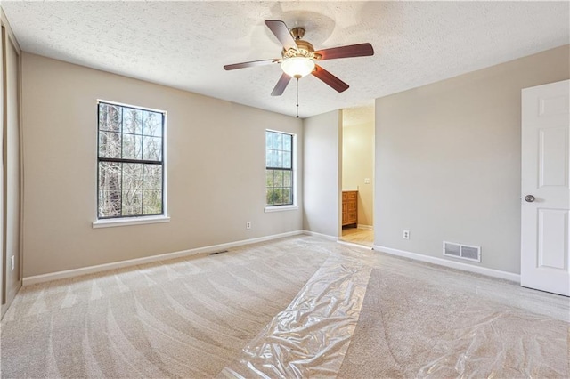 unfurnished bedroom with ensuite bathroom, light colored carpet, ceiling fan, and a textured ceiling