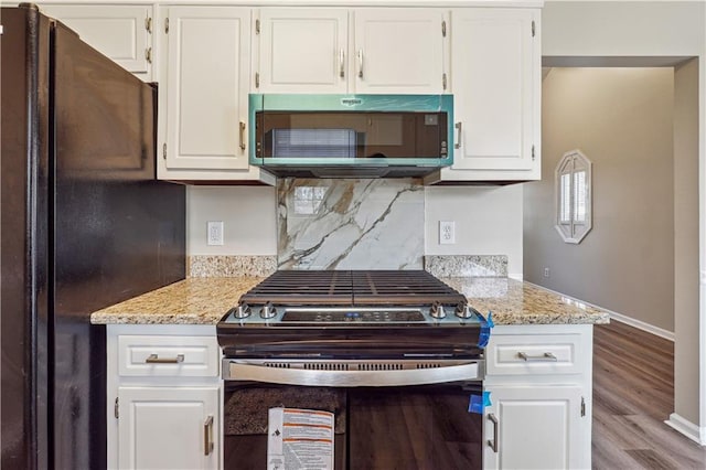 kitchen featuring black refrigerator, light stone counters, gas range, and white cabinets