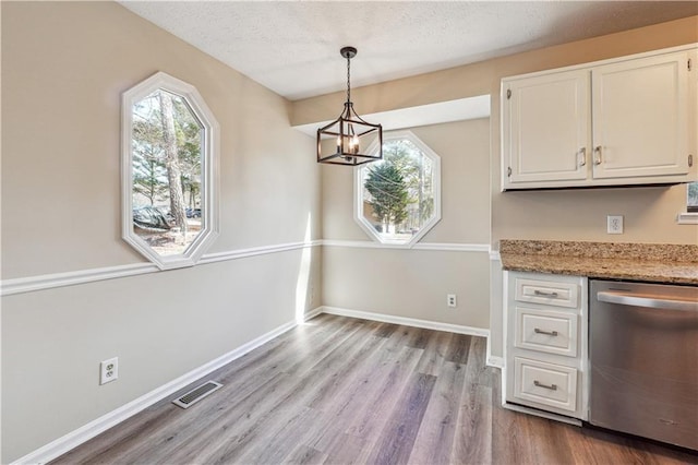 unfurnished dining area featuring an inviting chandelier, a textured ceiling, and light hardwood / wood-style flooring