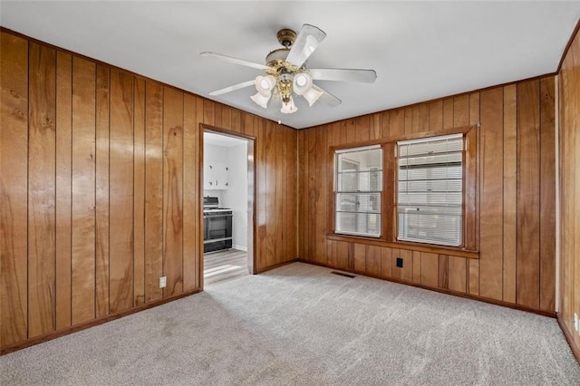 unfurnished room featuring wood walls, ceiling fan, visible vents, and carpet flooring