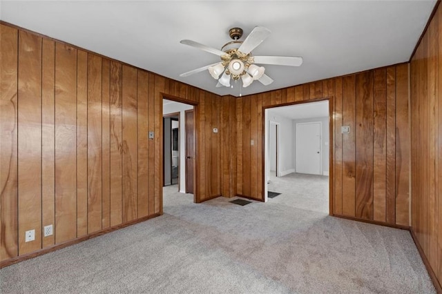 carpeted empty room with a ceiling fan and wooden walls