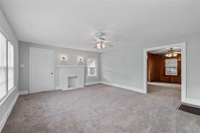 unfurnished living room featuring a brick fireplace, carpet, baseboards, and a ceiling fan