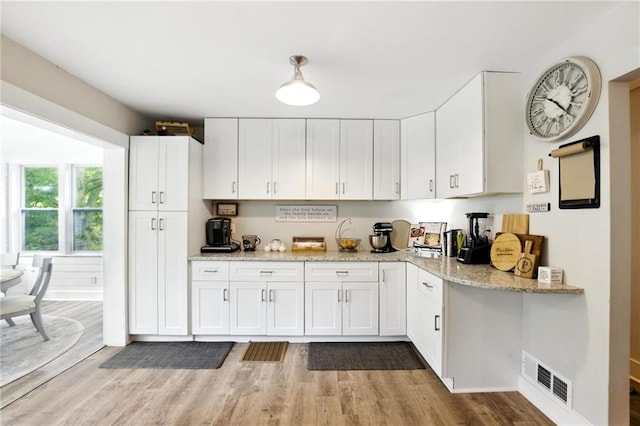 kitchen with light wood-style floors, white cabinets, and light stone countertops