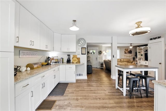 kitchen with light wood finished floors, white cabinetry, light stone counters, and a ceiling fan