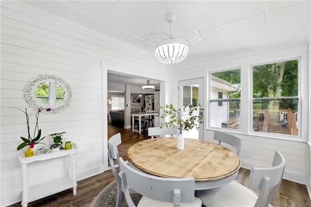dining room featuring a chandelier, dark wood-style floors, and wood walls