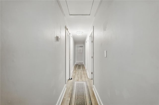 corridor with light wood-type flooring and baseboards