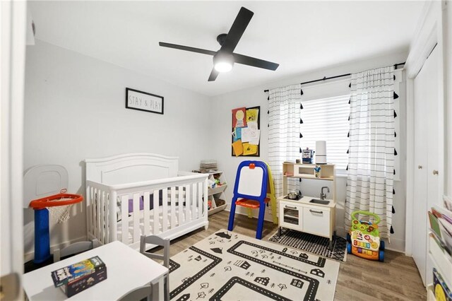 bedroom featuring light wood finished floors, a crib, and ceiling fan