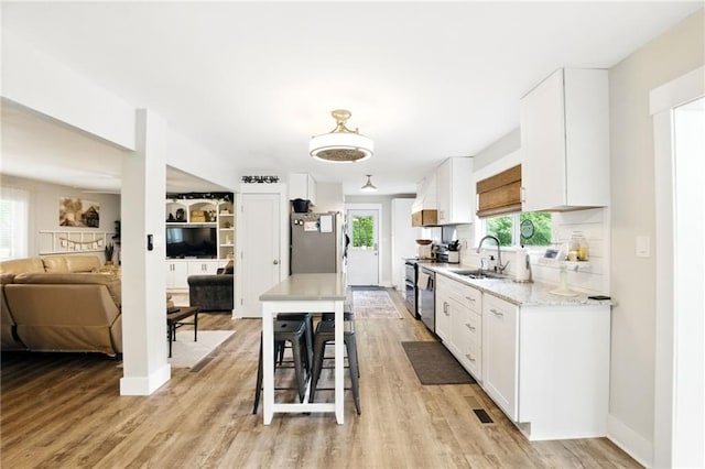 kitchen with appliances with stainless steel finishes, white cabinets, open floor plan, a sink, and light wood-type flooring