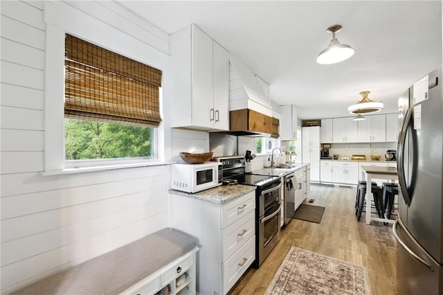 kitchen featuring appliances with stainless steel finishes, light wood-type flooring, a sink, custom range hood, and white cabinetry