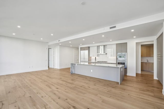 kitchen with gray cabinetry, a spacious island, sink, wall chimney range hood, and light hardwood / wood-style flooring