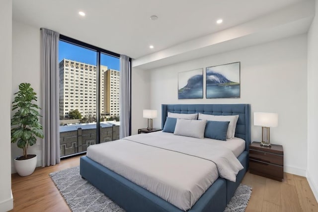 bedroom featuring access to exterior, light hardwood / wood-style flooring, and floor to ceiling windows