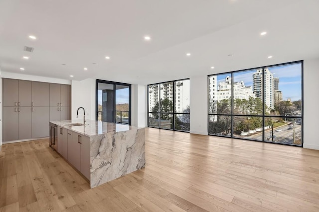 kitchen featuring a large island, sink, a wall of windows, light stone counters, and light hardwood / wood-style floors