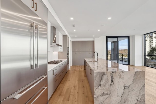 kitchen featuring wall chimney range hood, sink, a large island, light stone counters, and stainless steel appliances